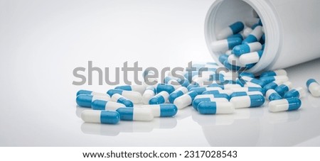 Blue-white antibiotic capsule pills spread out of plastic drug bottles. Antibiotic drug resistance. Prescription drugs. Healthcare and medicine. Pharmaceutical industry. Pharmacy product. Medication.