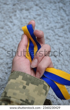 a blue-yellow ribbon in the hands of a military woman