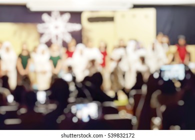 Blur Abstract Background Audience In Hall Of His Schoolchildren Play For Christmas Program On Stage Concert At School Or Church, Festival. Parents Watching Students Performance For New Year Fastive.