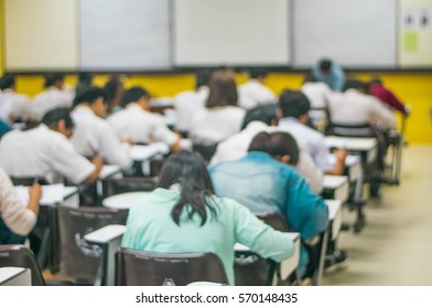 Blur Abstract Background Of Examination Room With Undergraduate Students Inside. Blurred View Of Student Doing Final Test In Exam Hall. Blurry View Of Study Chairs In Classroom Of University Or Campus