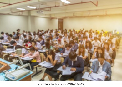 Blur Abstract Background Of Examination Room With Undergraduate Students Inside. Blurred View Of Student Doing Final Test In Exam Hall. Blurry View Of Study Chairs In Classroom Of University Or Campus