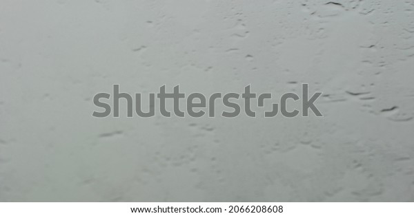 Blur abstract photo of drizzling rain under\
depression monsoon period in Thailand at the car windscreen,\
droplets are sticked at the glass in front of the car while in\
stuck in traffic jam at\
road