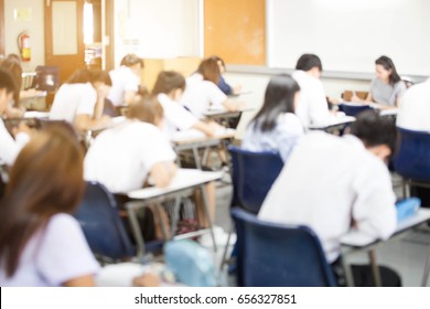 Blur Back View Abstract Background Of Examination Room With Undergraduate Students Inside. University Student In Uniform Sitting On Lecture Chair Doing Final Exam Or Study In Classroom.