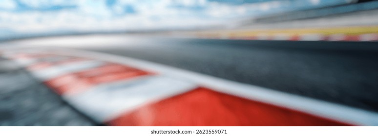 Blur Background of Dynamic Perspective of a Racing Track with Curved Asphalt and Vibrant Red and White Curbs Under a Cloudy Sky. Defocused Image for Background.