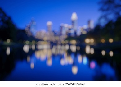 Blur Background of Nighttime Cityscape Reflection Over Calm Water with Illuminated Skyscrapers and Lush Green Parkscape. Defocused Image for Background.