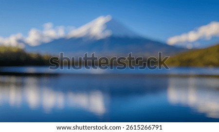 Blur Background of Snow-Capped Mountain Reflection on Calm Lake Under Clear Blue Sky with Fluffy White Clouds. Defocused Image for Background.