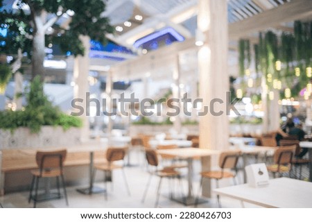 Blur bokeh background of interior table and chair in mall canteen. Abstract bokeh of food business dining court with no person, defocused of light retail lifestyle cafe shop decoration in modern.