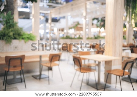 Blur bokeh background of interior table and chair in mall canteen. Abstract bokeh of food business dining court with no person, defocused of light retail lifestyle cafe shop decoration in modern.