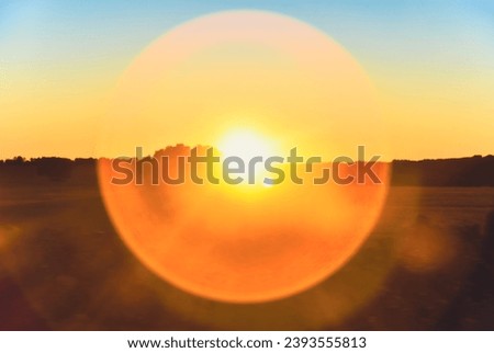 Blur bright orange sundog over fields. Orange circular halo around a bright afternoon sun.