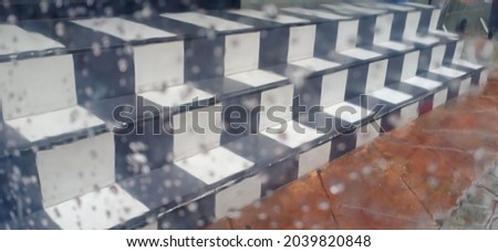 A blur of clear plastic panels with raindrop. It has stairways that alternate white and black square tiles in the background on the outside.