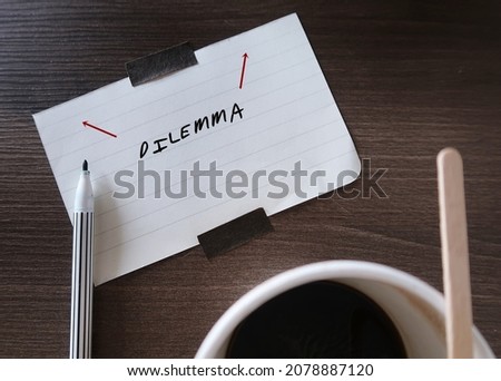 Blur coffee cup, pen on note paper written DILEMMA, concept of to choose between two tough choices, difficult decision making between alternatives equally undesirrable ones