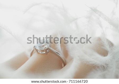 Blur of an elegant diamond ring on female finger with feather and sunlight tone, love and wedding concept.