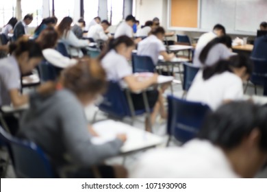 Blur Focus.back View Abstract Background Of Examination Room With Undergraduate Students Inside. University Student In Uniform Sitting On Lecture Chair Doing Final Exam Or Study In Classroom.