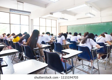 Blur Focus.back View Abstract Background Of Examination Room With Undergraduate Students Inside. University Student In Uniform Sitting On Lecture Chair Taking Final Exam Or Study In Classroom.