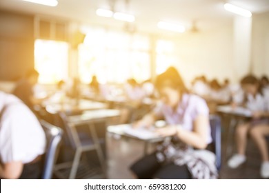 Blur Front View Abstract Background Of Examination Room With Undergraduate Students Inside. University Student In Uniform Sitting On Lecture Chair Doing Final Exam Or Study In Classroom.