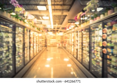 Blur Frozen Food Section At Retail Store In US. Huge Glass Door Aisle With Variety Pack Of Processed Fruit, Vegetable, Breakfast, Appetizer, Side, Meals , Pizza. Top Orchid Row Decoration.Vintage Tone