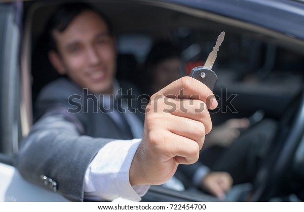 Blur of Happy smiling man\
showing car key from in car.Focus on the key.Auto business and car\
sale for consumerism and people concept.In selective\
focus