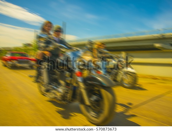blur image. Biker Couple with motorcycle Chopper.\
Man and woman ride with high speed Cute girl wear black leather\
jacket and stylish sunglasses against urban background Gang of\
groups of armed people