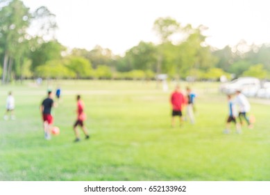 Blur Image Group Of Latin America Kids Playing Football With Coach On Green Soccer Pitch In Park At Sunset Warm Light In Humble, Texas. Urban Healthy Lifestyle Concept. Boys Kicking Football On Field.