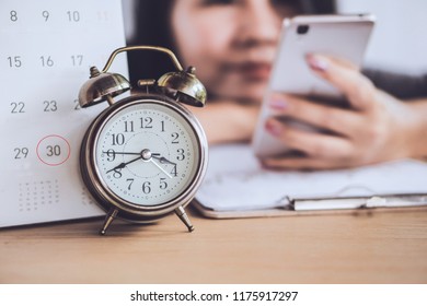 Blur Lazy Woman Worker Wasting Time At Work Using Smart Phone With Alarm Clock And Deadline Calendar On Office Desk