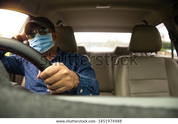Blur male wearing a face mask, black glasses,\
and a black hat. Closeup hands of a man holding the steering wheel\
to control the car, are Upset while traffic congestion daylight.\
Blurred background