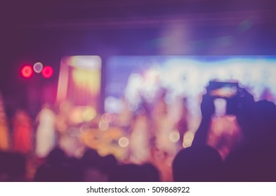 Blur People Taking Smart Phone In Night Outdoor Concert With Colorful Bokeh Abstract Background. Activity And Lifestyle Concept. Vintage Tone Filter Color Style.