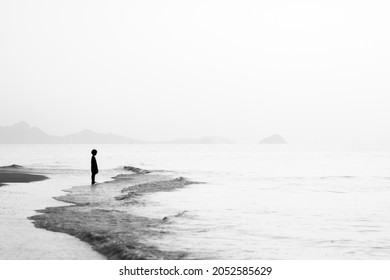 Blur photo of silhouette of a lonely boy standing at the beach looking at the sea.