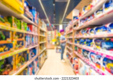 Blur Toy Store Interior As Background With Copy Space. Defocused Shelves With Many Toys. Blurred Teenage Boy Choosing Birthday Gift At Toy Market 