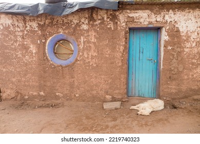 Blur, Turquoise Wooden Door And A Blue  Tire As Window, White Dog Sleeping At The Door Step, Mud House In San Pedro De Atacama, Northern Chile