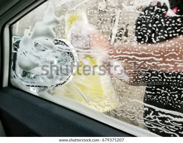 blur view of male foreign worker rubbing soap with\
soft sponge on the car windshield wind screen at a local automotive\
car-wash center