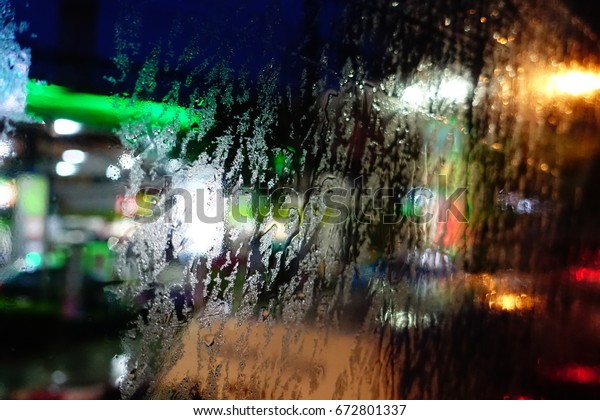 Blur window glass art by rain drops and city\
light in the evening outside\
