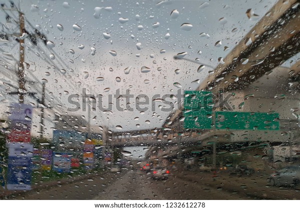 Blured background with rains drop on\
glass and cars on the road in rainy weather. Road view through car\
window blurry with heavy rain. Driving in rain.\
