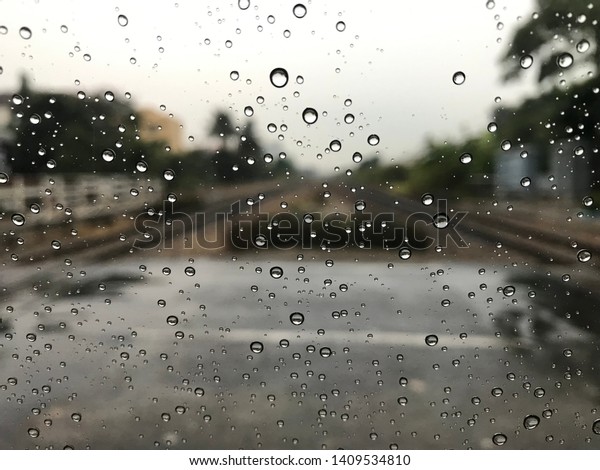 Blured background with rains drop on\
glass and cars on the railway, Road view through railway window\
blurry with heavy rain, Driving in rain, rainy\
weather