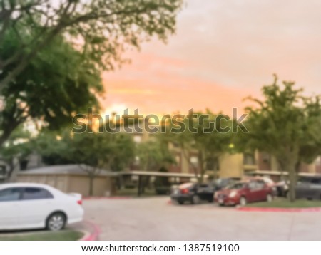 Blurred abstract apartment complex with detached garage and covered parking lots in Texas, America. Row of parked cars under dramatic sunset cloud