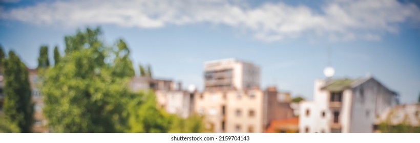 Blurred Abstract City Background, Blue Sky Buildings And Green Trees. Banner Format