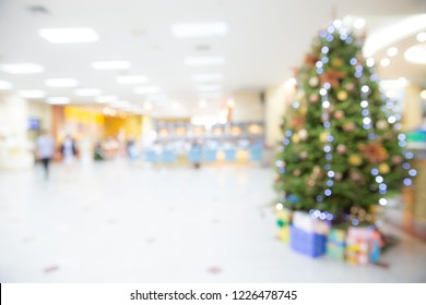 Blurred Abstract Of Decorated Christmas Tree With Toys, Gift Box And Bauble Inside The Office Building Or Hospital. Chritmas And Happy New Year Concept. Bokeh Lights.