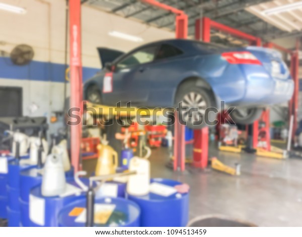 Blurred abstract mechanic changing oil below of\
lifted car at auto shop in Texas, USA. Defocused background\
interior of modern oil change service station. Working technician\
at garage concept