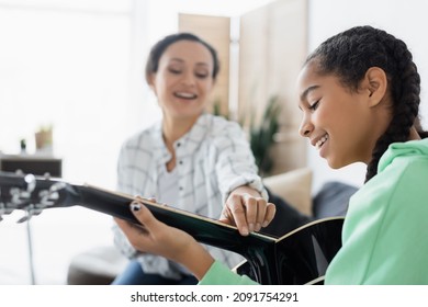 blurred african american woman touching strings on guitar near smiling daughter - Powered by Shutterstock