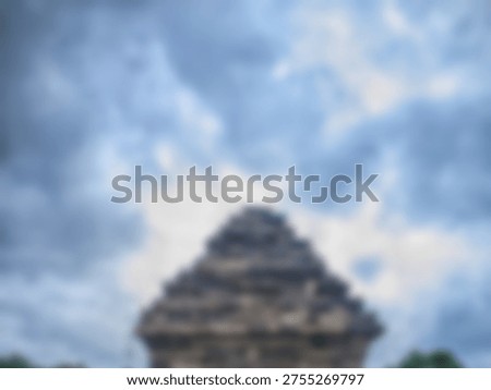 Blurred ancient stone temple structure top seen dramatically against a dark, moody cloudy sky.