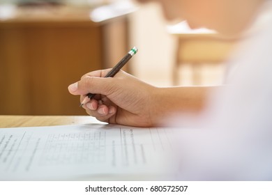 Blurred of Asian boy students hand holding pencil writing fill in Exams paper sheet or test papers on wood desk table with student uniform in exam class room, education concept - Shutterstock ID 680572507