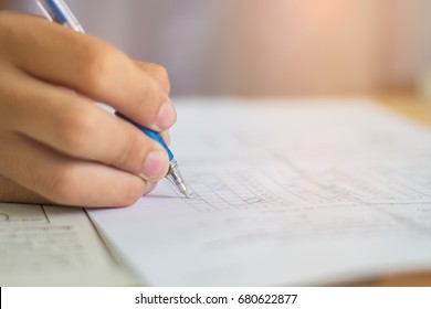 Blurred Of Asian Boy Students Hand Holding Pen Writing Fill In Exams Paper Sheet Or Test Paper On Wood Desk Table With Student Uniform In Exam Class Room, Education Concept, Thailand