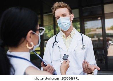 Blurred Asian Reporter Holding Voice Recorder Near Doctor In Medical Mask And White Coat