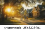 Blurred Background of Children Riding Bicycles on a Suburban Street at Sunset with Warm Golden Light and Charming Houses in the Background. Blurry Background For Design Projects.