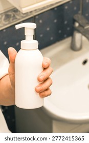 Blurred background emphasizing hand grasping unlabeled bottle in bathroom environment.