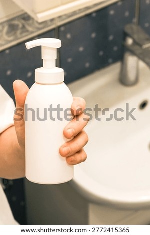 Blurred background emphasizing hand grasping unlabeled bottle in bathroom environment.