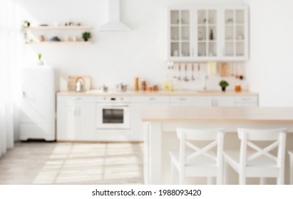 Blurred Background With Family Dining Room And Minimalist Kitchen Interior. Wooden Table, Kitchenware And Utensils On Furniture And Shelves, White Walls