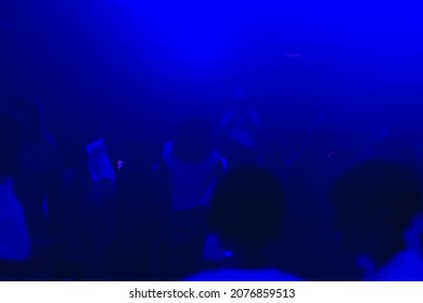 Blurred background with figures of dancing blurry people at a disco with blue lighting.