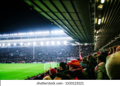 Blurred background of football players playing and soccer fans in match day on beautiful green field with sport light at the stadium. Sports,Athlete,People Concept.Mercy Side,Anfield,Liverpool.UK