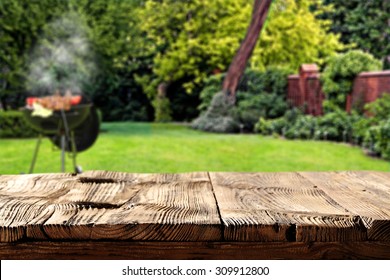 blurred background of green garden with grill time and shabby dark brown table of picnic 