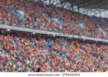 A blurred background of a large crowd of spectators sitting in the stands of a sports stadium during an event.